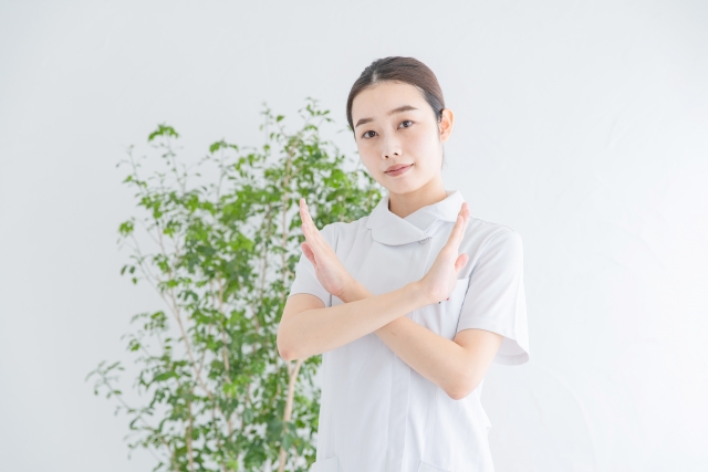 白衣を着た女性が胸の前でバツマークを作っている画像
