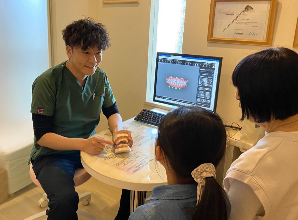 歯科医師が歯の模型とモニターを使って患者さまに説明している様子の写真